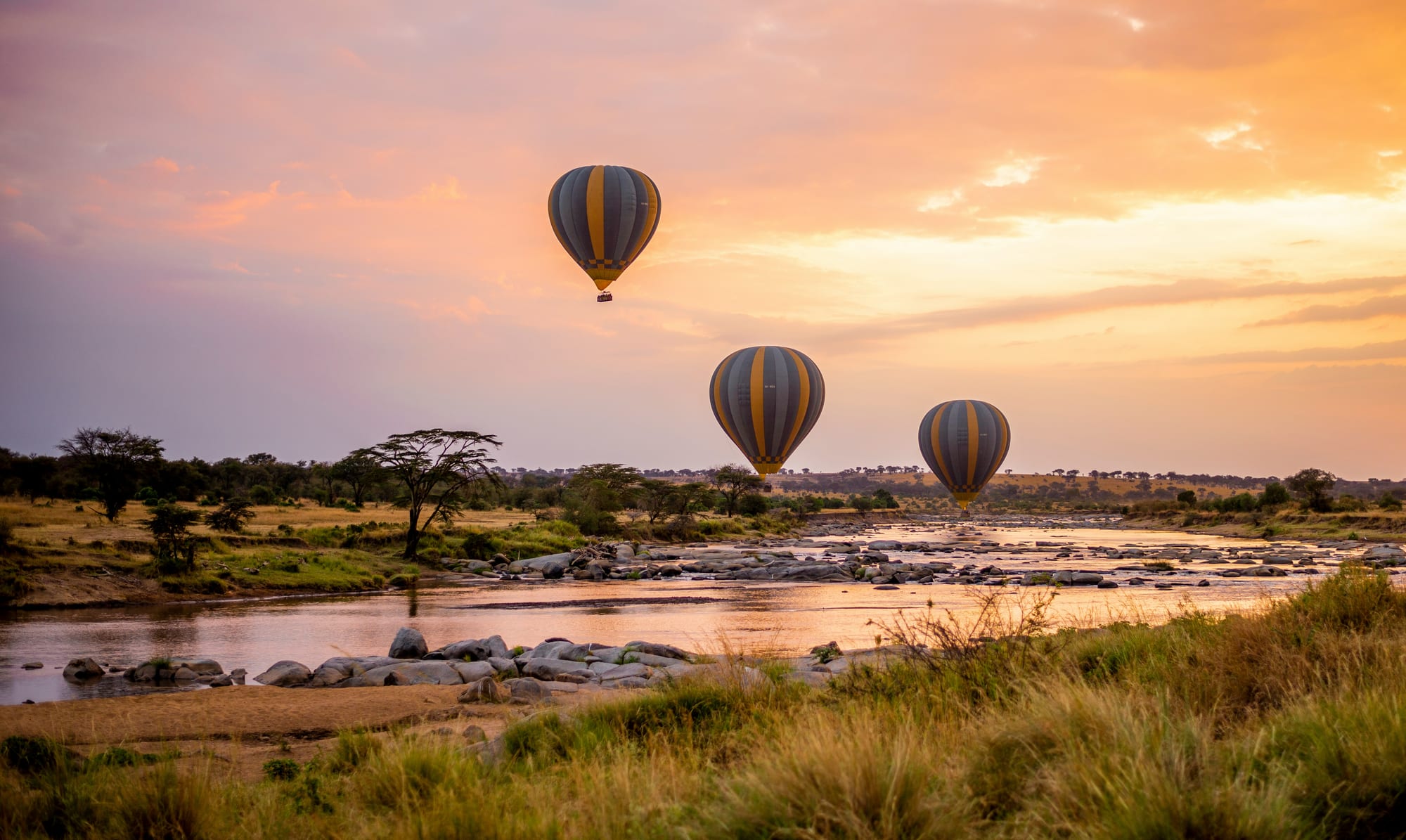 Hot air balloons drifting above a river at sunrise
