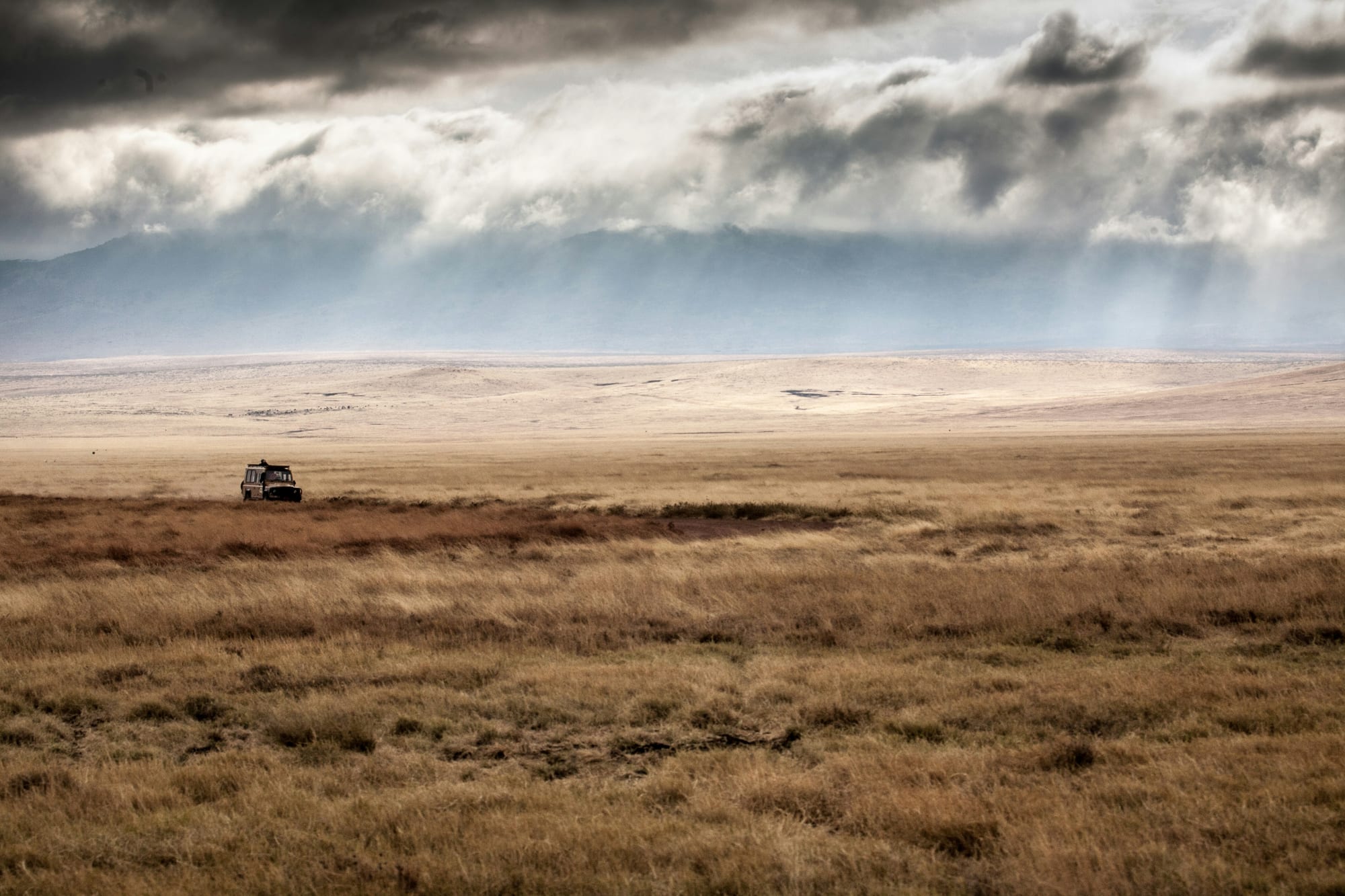 A single safari vehicle crossing the Ngorongoro Crater floor under storm cloud
