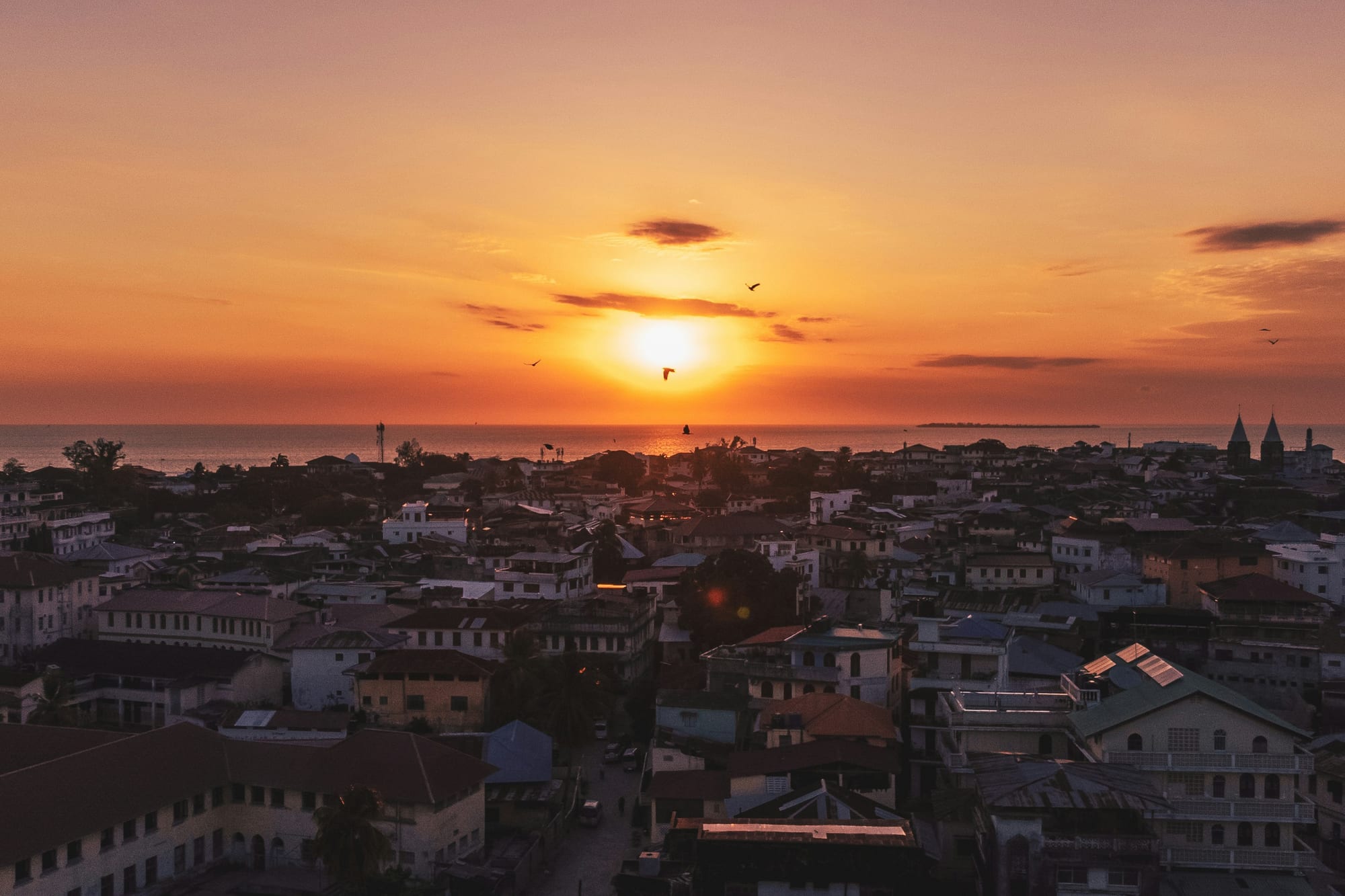 Sun setting over the rooftops of a coastal town beside the sea