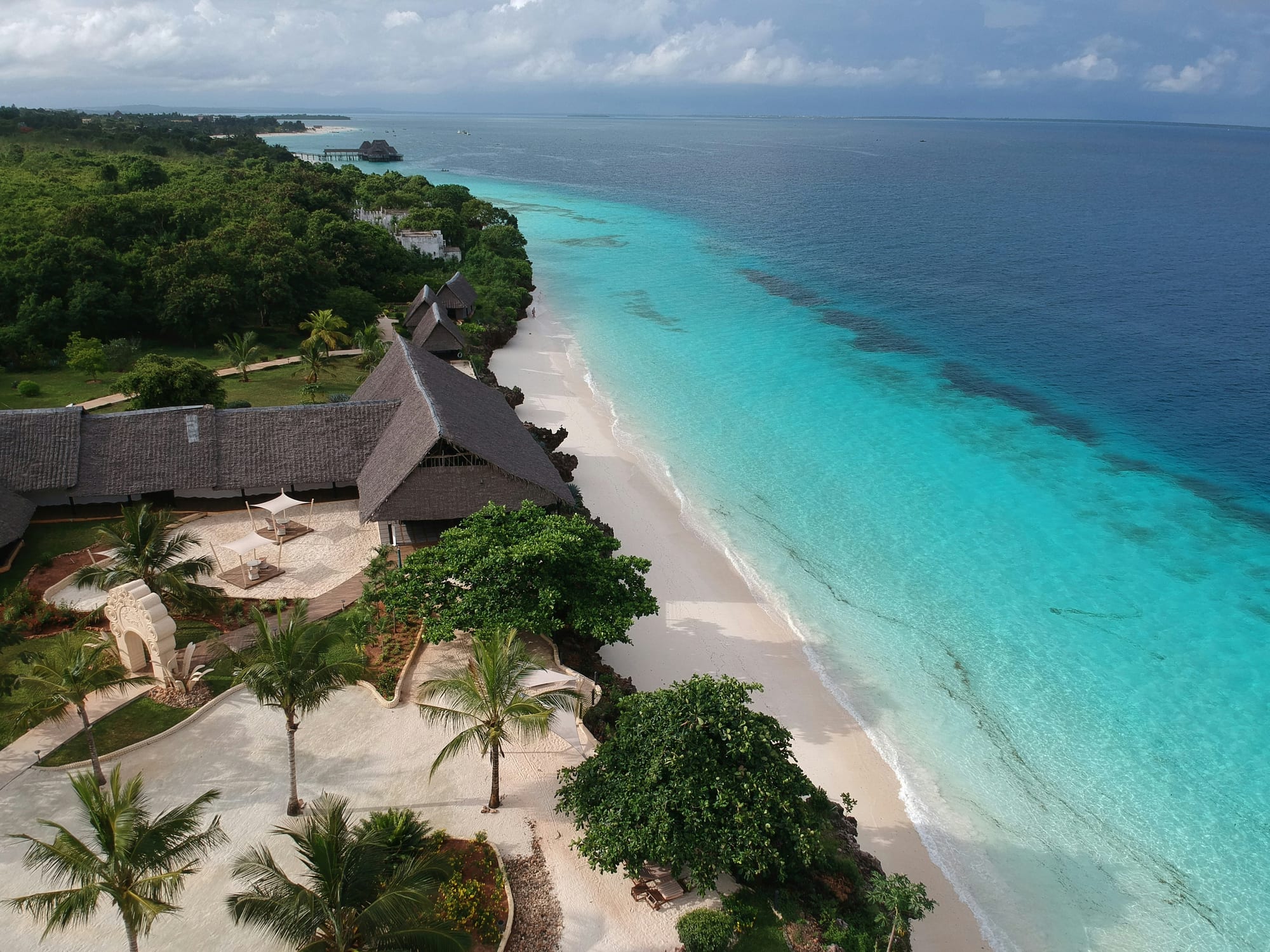 Thatched buildings and palms above a white sand beach and turquoise shallows